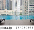 Young asian woman relaxing by pool at Kuala Lumpur hotel with view of surrounding skyscrapers, enjoying leisure time in vibrant urban setting. 134239363