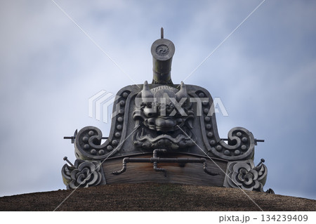 An ancient Japanese temple roof is adorned with an Onigawara carved with striking detail An ancient Japanese temple roof is adorned with an Onigawara carved with striking detail 134239409