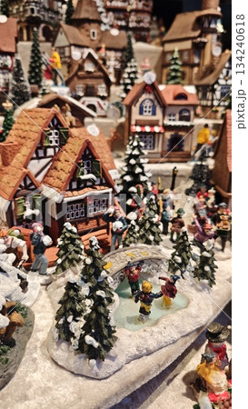 Cozy miniature Christmas village with snow covered houses, pine trees and people skating on a frozen pond. The image represents holiday tradition, nostalgia, winter celebration and festive atmosphere Cozy miniature Christmas village with snow covered houses, pine trees and people skating on a frozen pond. The image represents holiday tradition, nostalgia, winter celebration and festive atmosphere 134240618