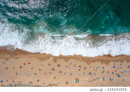 Tourists and parasols on sandy seashore with waves 134241059