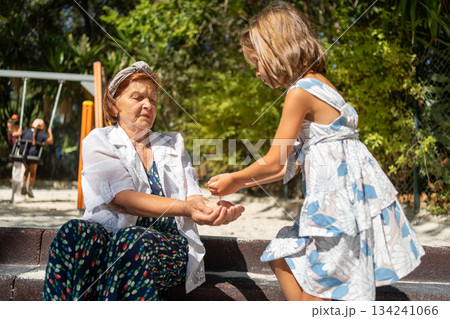 Girl pouring sand into grandmother hands at 134241066
