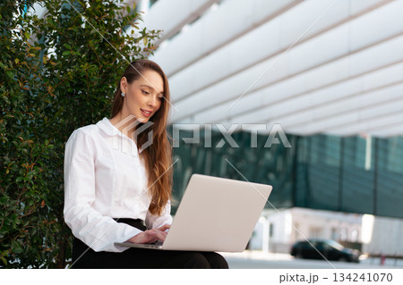 Businesswoman sitting outdoors working on laptop Businesswoman sitting outdoors working on laptop 134241070