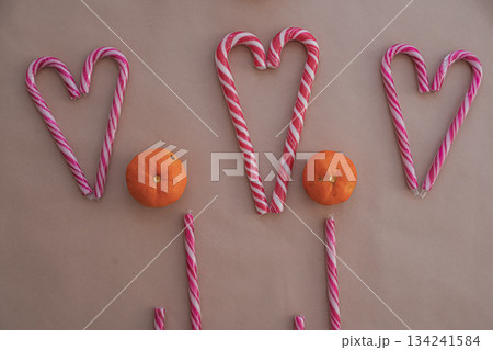 Three Heart-Shaped Candy Canes with Tangerines on Beige Background 134241584