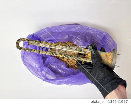 Plumber hand holding a boiler heating element covered with limescale, hard water residue, boiler maintenance and cleaning, scale removal, water heater repair 134241957