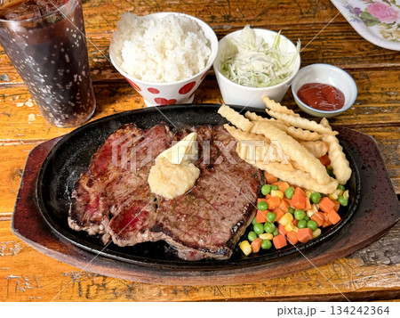 Juicy grilled steak served with french fries, rice, and mixed vegetables on a sizzling platter 134242364