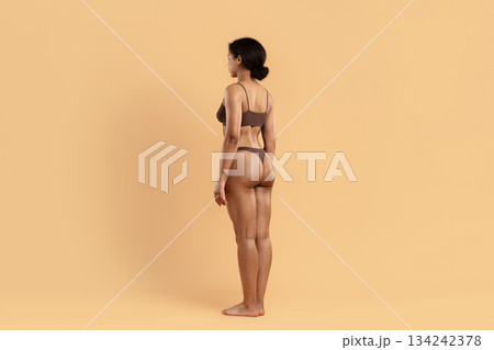 Side profile of young black woman in underwear standing on beige background Side profile of young black woman in underwear standing on beige background 134242378
