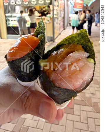 Hand holding two delicious temaki sushi rolls with salmon, uni, and shrimp 134242542