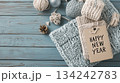 Top view of knits and yarn on wooden blue background with greeting "Happy New Year" on paper card. Cozy winter banner with knitting theme 134242783