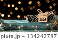 Festive New Year banner with garland, pine cones, paper tag with 2026 text, and golden bokeh lights on black background 134242787