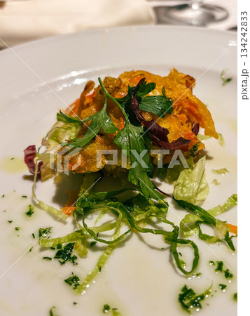 Gourmet appetizer of crispy fried bites with fresh salad greens and herbs, elegantly drizzled with olive oil on a white plate, refined presentation for fine dining 134242833