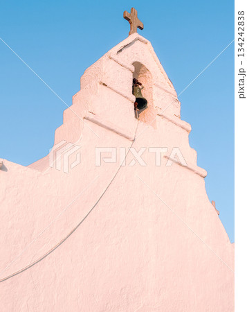 Mykonos chapel bell tower with a traditional wooden cross and a pale pink stucco facade, representing greek island architecture and spiritual travel destinations Mykonos chapel bell tower with a traditional wooden cross and a pale pink stucco facade, representing greek island architecture and spiritual travel destinations 134242838