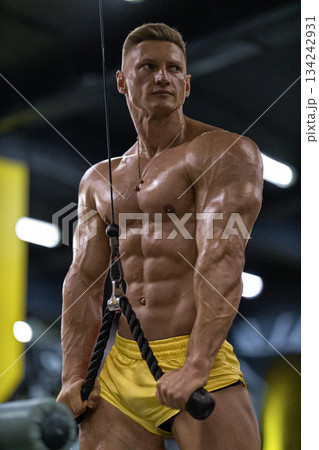 athlete performs exercises on a cable machine in a gym. He is focused on his workout pulling the handles while showing strength and muscle definition. 134242931