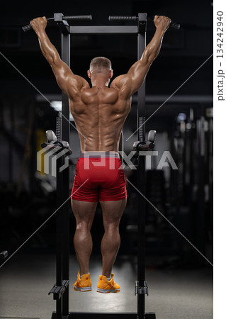 athlete works on strength by doing pull ups in a gym. This scene captures the dedication and focus required during an evening workout routine. 134242940
