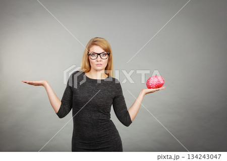 Woman in eyeglasses being confused holding brain 134243047