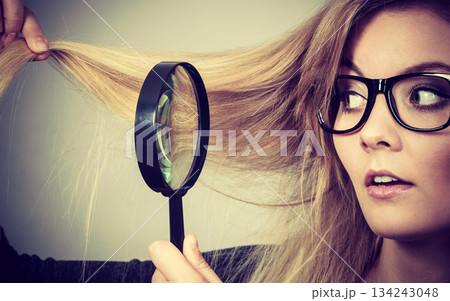 Woman holding magnifying glass looking at hair Woman holding magnifying glass looking at hair 134243048