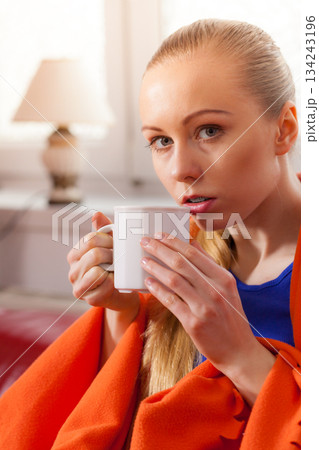 Woman lying on sofa under blanket drinking tea 134243196