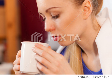 Woman lying on sofa under blanket drinking tea 134243197