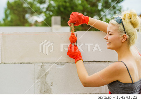 Woman using string as level in wall construction. 134243322