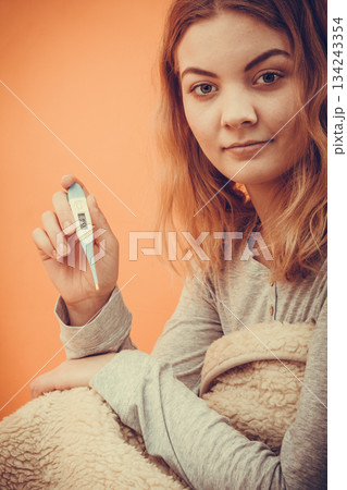 Sick woman under blanket with digital thermometer. 134243354