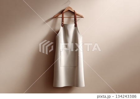 White apron mockup, simple uniform hanging on a wooden hanger with leather straps against a smooth beige wall. Blank apparel template, clean design for a commercial kitchen or coffee shop. 134243386