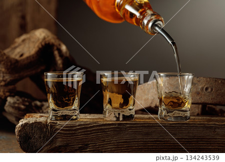 Whiskey is poured from a bottle into a shots. Whiskey is poured from a bottle into a shots. 134243539