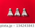 Three White Feather Shuttlecocks Arranged In A Row Against A Bold Red Background 134243843