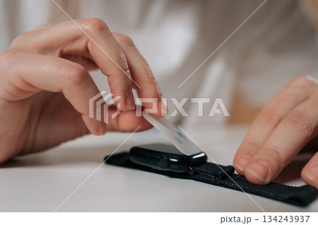 Closeup of woman applying protective film to smartwatch screen, hands placing transparent accessory on digital display for scratch and damage resistance, ensuring gadget longevity. Closeup of woman applying protective film to smartwatch screen, hands placing transparent accessory on digital display for scratch and damage resistance, ensuring gadget longevity. 134243937
