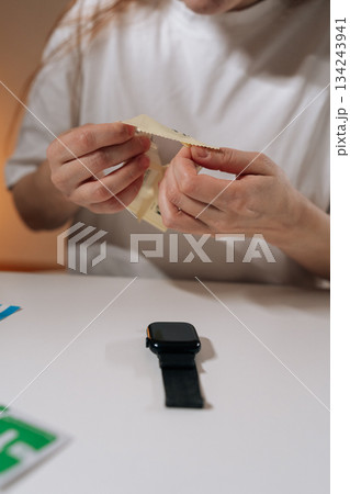 Vertical cropped shot of person preparing screen protector for smartwatch, ensuring device care and maintenance, protecting technology from scratches and daily wear, extending gadget lifespan. 134243941