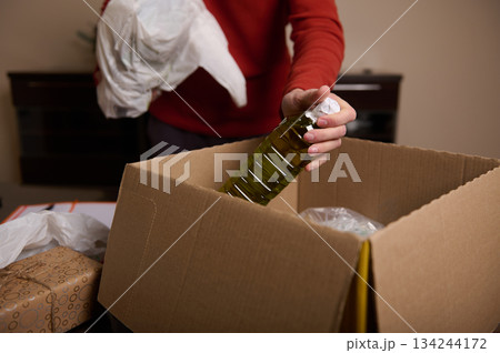 Person Packing Olive Oil Bottle Into Cardboard Box For Shipping Or Moving Person Packing Olive Oil Bottle Into Cardboard Box For Shipping Or Moving 134244172