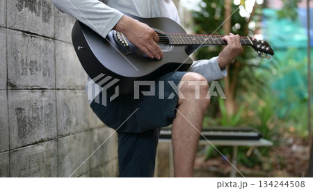 Black Acoustic Guitar With Gray Shirt Hand Playing, Against Gray Wall Green Outdoor Background, Alternative Sound Black Acoustic Guitar With Gray Shirt Hand Playing, Against Gray Wall Green Outdoor Background, Alternative Sound 134244508