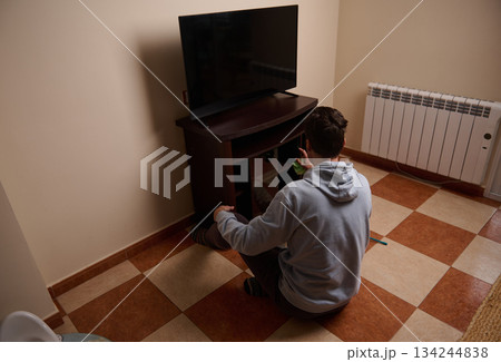 Person Sitting on Floor Watching TV in Living Room With Hoodie and Remote Person Sitting on Floor Watching TV in Living Room With Hoodie and Remote 134244838