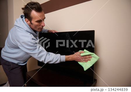 Man Wiping Flat Screen TV With Green Cloth In Living Room 134244839