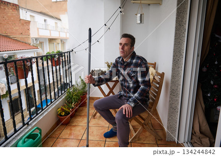 Man On Balcony With Monopod Looking Thoughtful In Plaid Shirt During Christmas Season 134244842