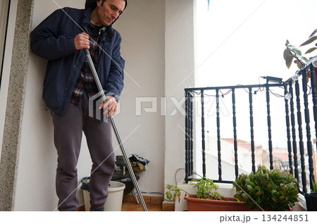Man With Mop On Balcony Cleaning, Plants, and Morning Light Outdoors 134244851