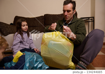 Family At Home Packing Trash Bags: Father Sealing Garbage While Kids Watch Together During Evening 134244885
