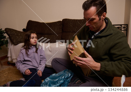 Father Opening A Cardboard Gift Box While Daughter Watches In Cozy Living Room 134244886
