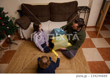 Family Christmas Gift Exchange At Home With Father And Children On Rug In Living Room Family Christmas Gift Exchange At Home With Father And Children On Rug In Living Room 134244889