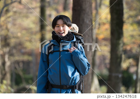 秋冬の紅葉の山を登山をする若い男性カメラ目線　アウトドアのお出かけやレジャーのイメージ	 134247618