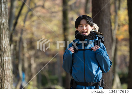 秋冬の紅葉の山を登山をする若い男性カメラ目線　アウトドアのお出かけやレジャーのイメージ	 134247619