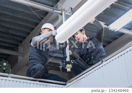 天井が近い高所の足場で単管パイプを固定するクランプなどの施工作業　鳶職や作業員のイメージ 134248468