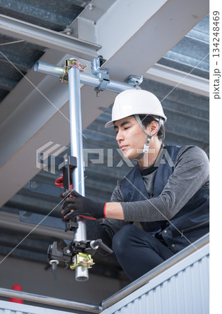 天井が近い高所の足場で単管パイプを固定するクランプなど施工作業　鳶職や作業員イメージ　レンチで締める 134248469