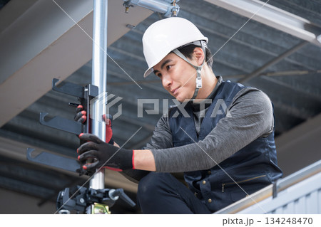 天井が近い高所の足場で単管パイプを固定するクランプなど施工作業　鳶職や作業員イメージ　レンチで締める 134248470