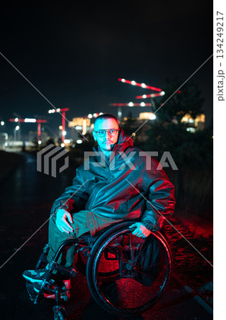 Man with disability in wheelchair in red blue rgb color light on late night walk alone in urban city 134249217