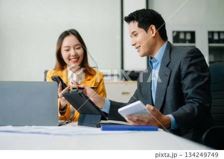 Two asian business workers talking on the smartphone and using laptop at office. 134249749