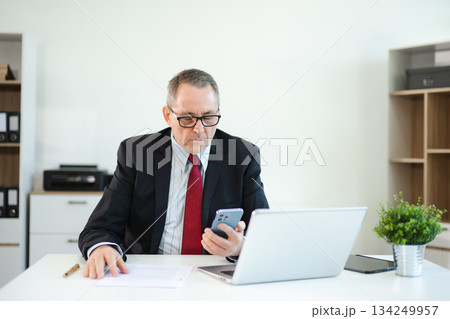 Confident businessman in suit, working on laptop and smartphone at office desk. Professional executive, leadership, strategy 134249957