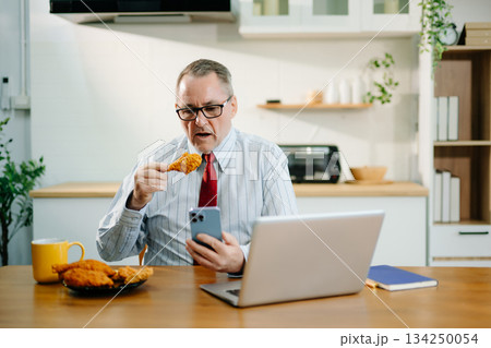 Mature Businessman using laptop while sitting at home. man sitting in kitchen and doing market research working Mature Businessman using laptop while sitting at home. man sitting in kitchen and doing market research working 134250054