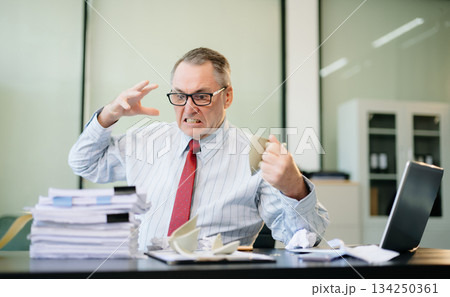 Angry and irritated Mature Businessman sitting in the office of laptop with his keyboard tired from work. Overwork, stress 134250361
