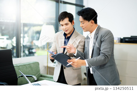 Two Asian businessmen using tablet and smartphone for project planning in a modern office. 134250511