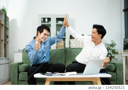 Joyful Asian businessmen celebrating success with high-five in office, symbolizing teamwork, victory Joyful Asian businessmen celebrating success with high-five in office, symbolizing teamwork, victory 134250521