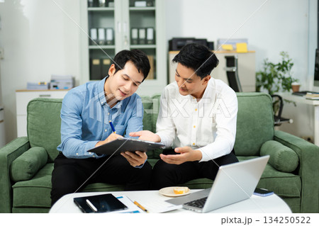 Two Asian businessmen smiling while signing a contract on clipboard, symbolizing business cooperation, teamwork Two Asian businessmen smiling while signing a contract on clipboard, symbolizing business cooperation, teamwork 134250522